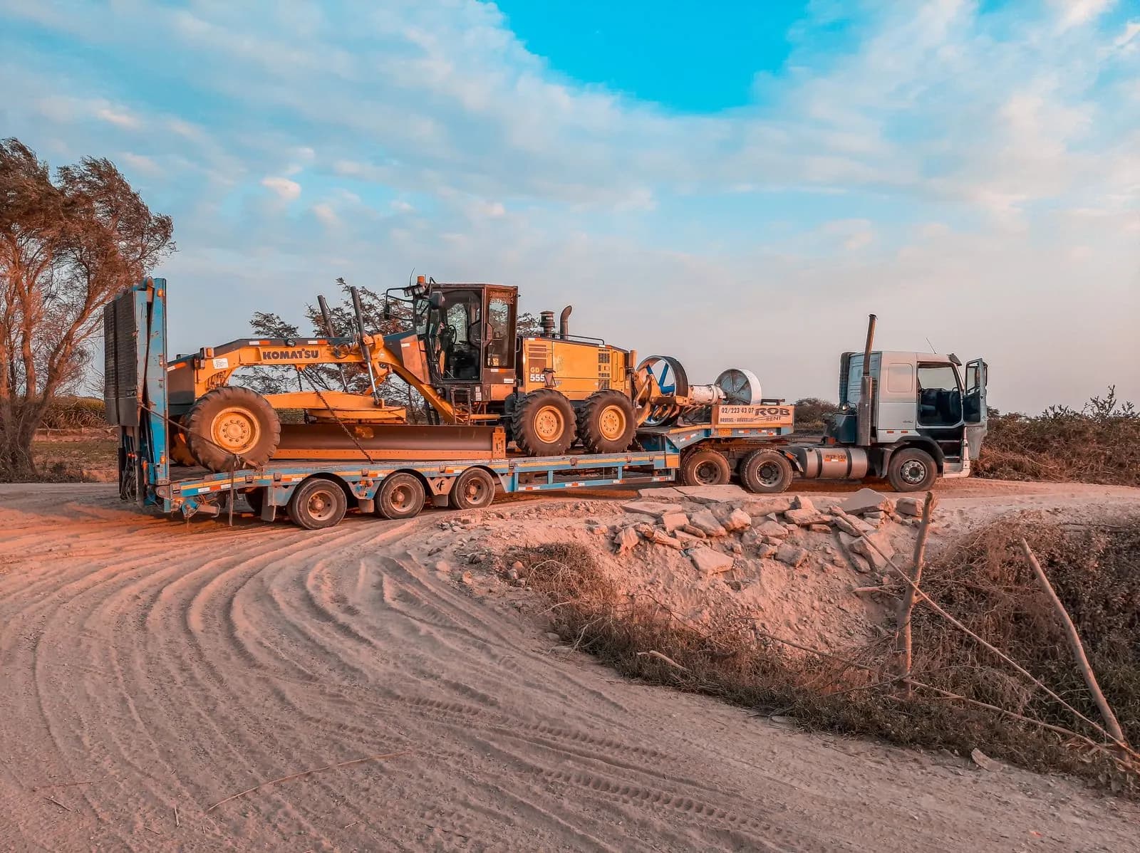 Flatbed trailer hauling heavy machinery on a dirt road